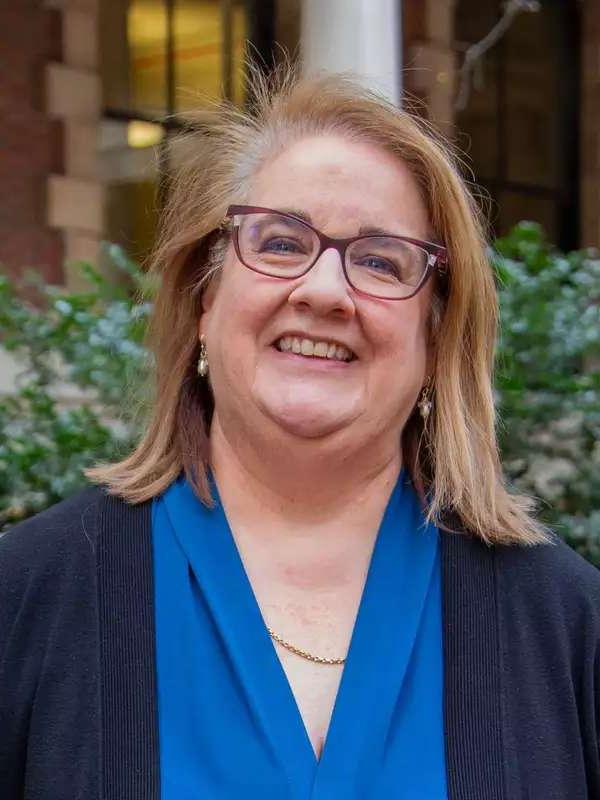 Christine smiling, wearing classes, blue blouse and navy blue sweater against a mixed background